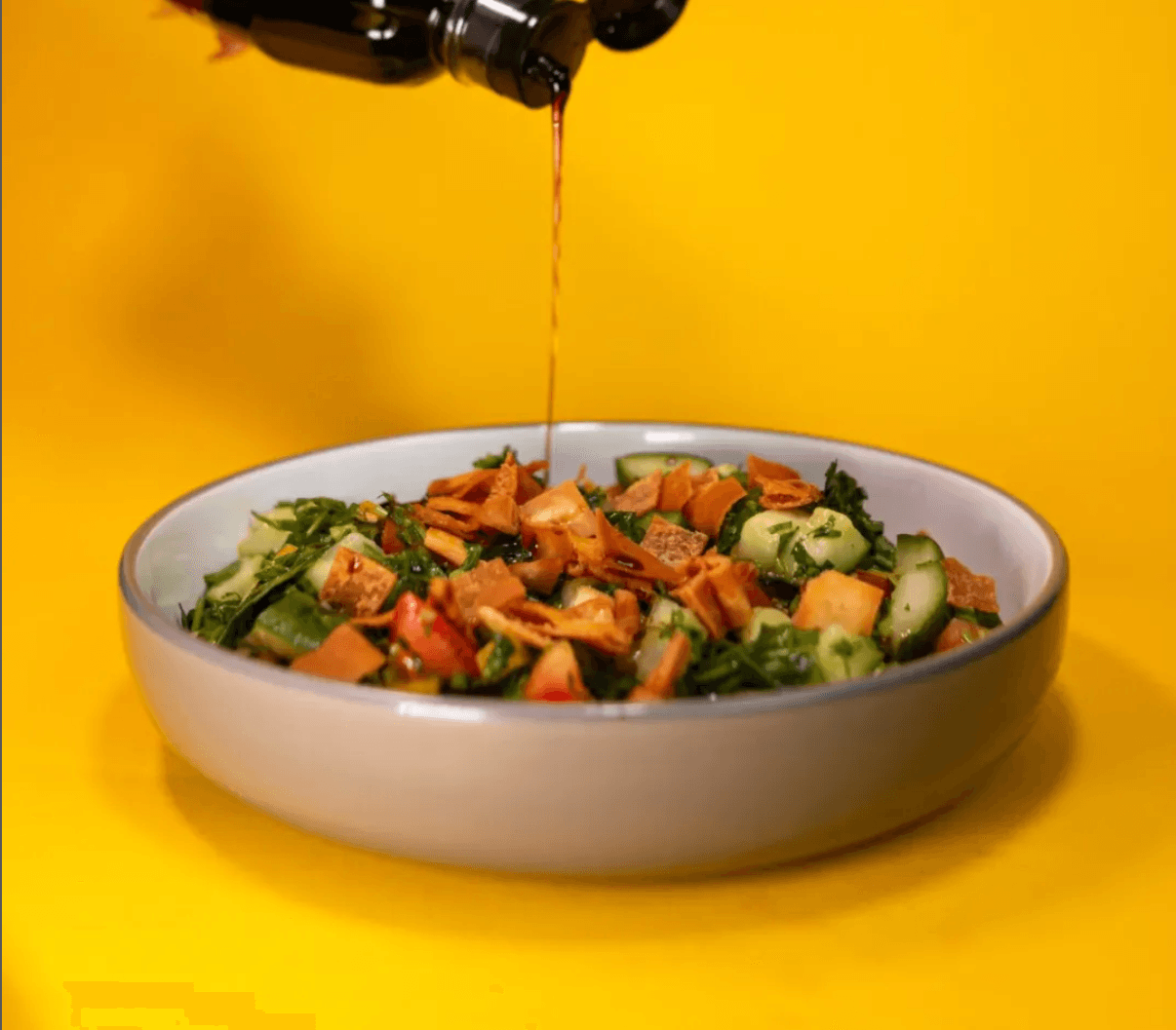 Pomegranate molasses poured over a bowl of fattoush salad